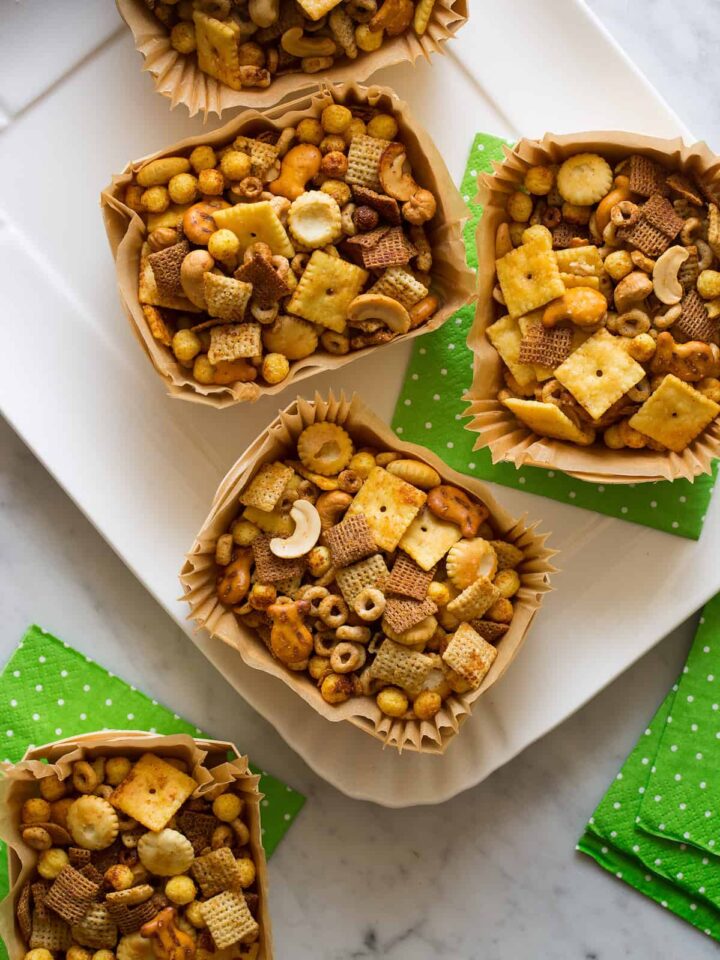 Wood and paper containers full of snack mix on a platter with green paper napkins.