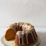 A pumpkin bundt cake topped with pistachio glaze and pistachios with a piece cut out.