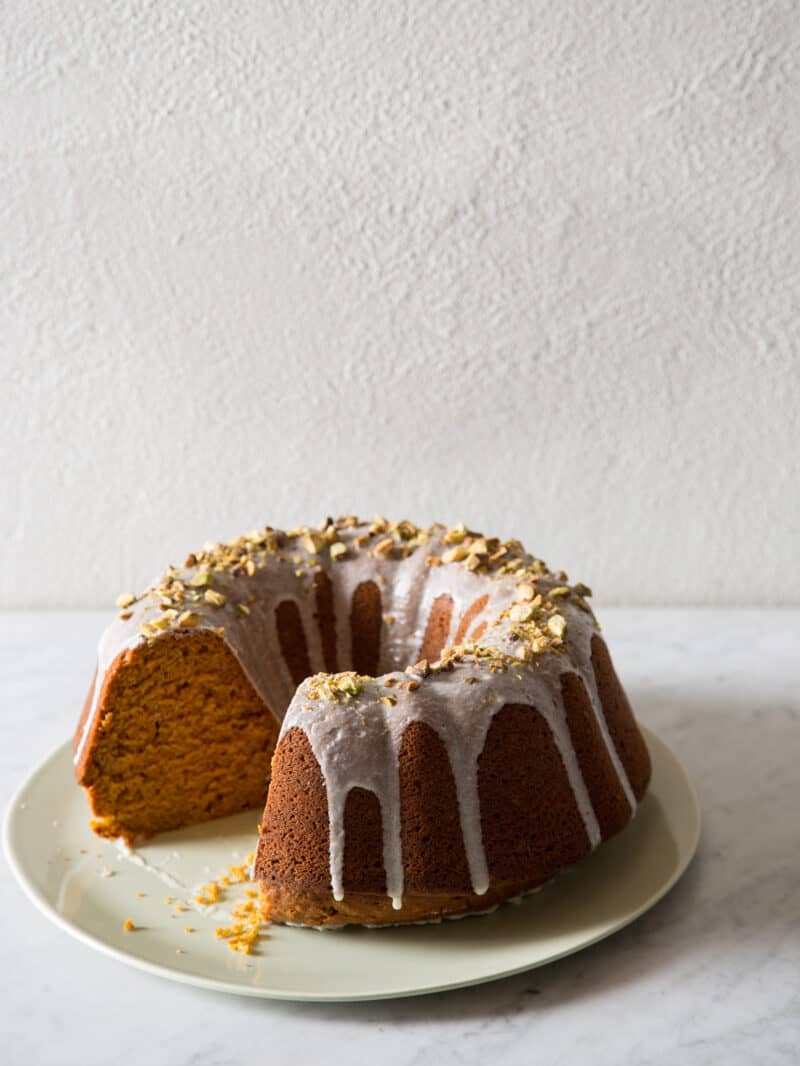 A pumpkin cake with pistachio glaze with a slice taken out.