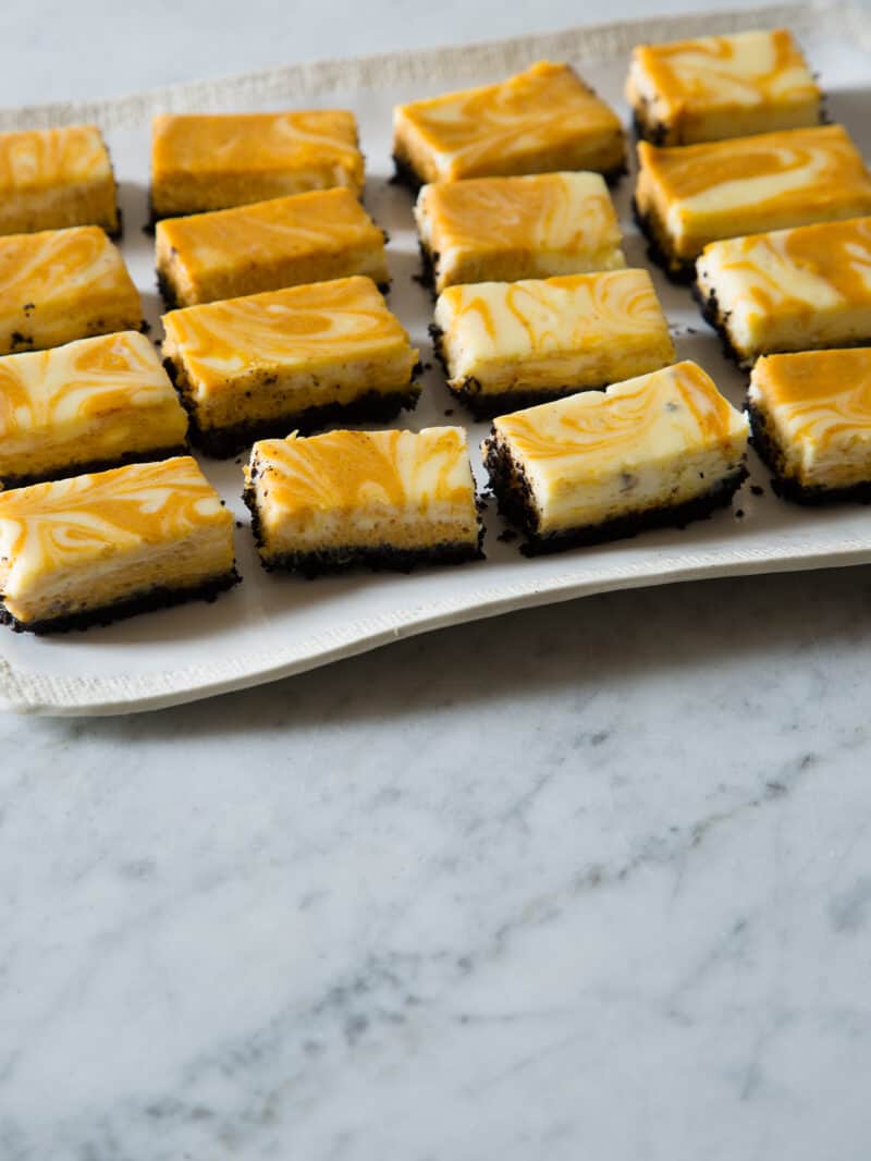 A close up of marbled pumpkin cheesecake bars cut and on a platter.