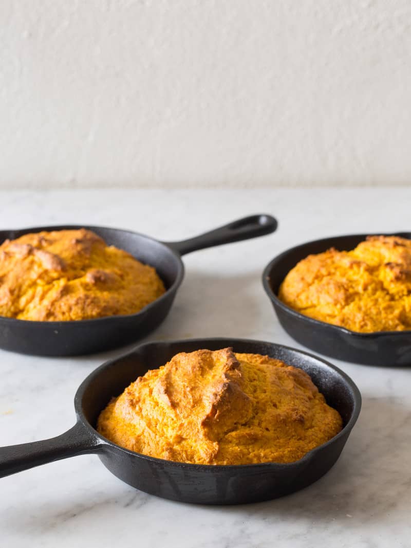 Three cast iron skillets with pumpkin cornbread.