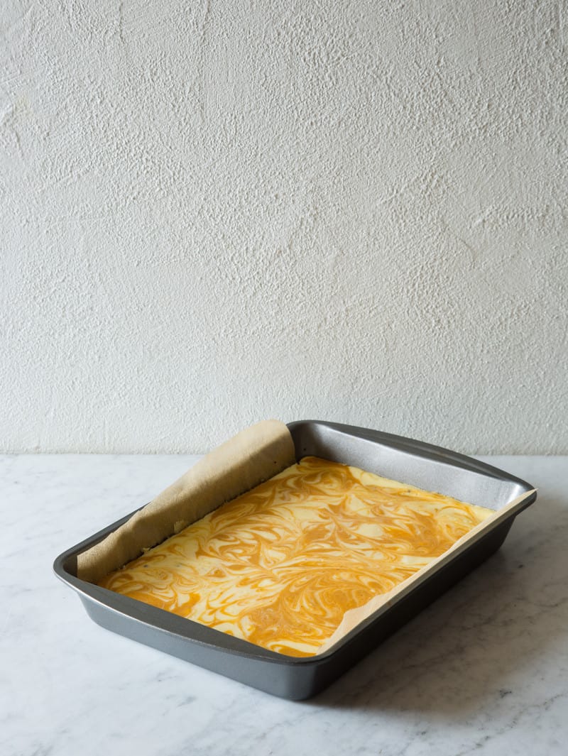 A lined pan of uncooked marbled pumpkin cheesecake.