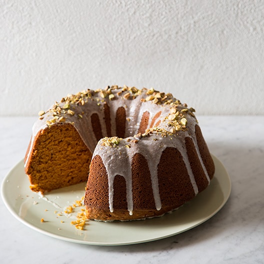 A whole pumpkin bunt cake with pistachio glaze with a slice taken out.