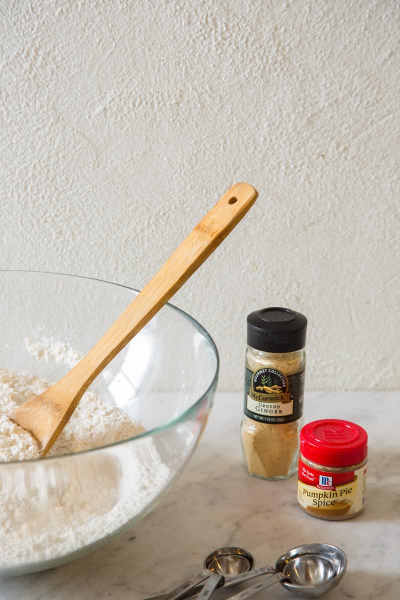 A large bowl of dry ingredients with a wooden spoon next to a few spice bottles.