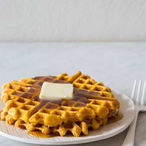 Stacked pumpkin spiced waffles with butter and syrup on a plate with a fork.