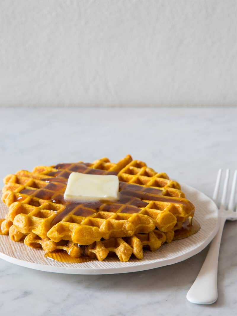 Stacked pumpkin spiced waffles with butter and syrup on a plate with a fork.