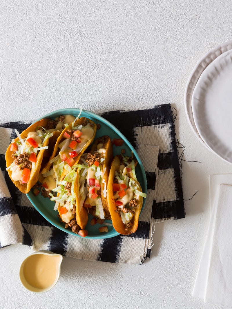 A plate of crunchy ground beef and cheesy tacos with napkins and extra plates.