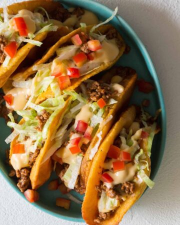 A plate of crunchy beef tacos with a cheese sauce on top.