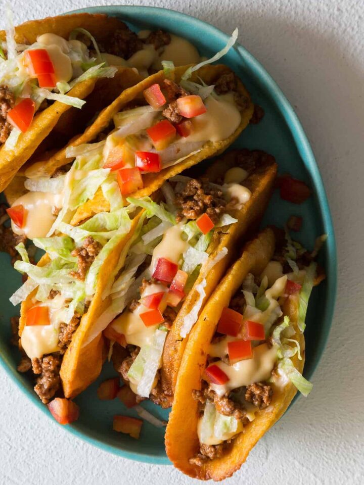 A plate of crunchy beef tacos with a cheese sauce on top.