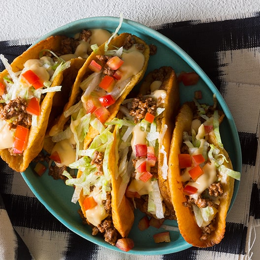 A plate of crunchy beef tacos with a cheese sauce on top.