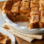 A close up of a whole brown butter apple pie with slice removed.