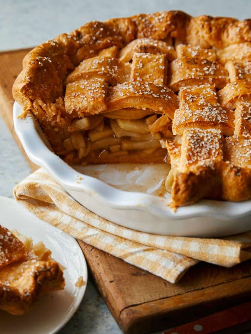 A brown butter apple pie with cheddar crust by a piece served on a small plate.