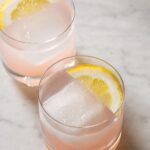 A close up of red grapefruit and rum spritzers garnished with lemon slices.