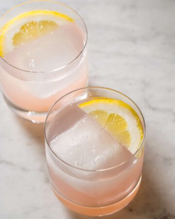 A close up of red grapefruit and rum spritzers garnished with lemon slices.