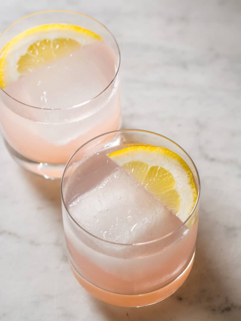 A close up of rum spritzers with lemon slices on a marble surface.