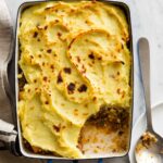 A baking pan of sweet potato shepard's pie with a portion taken out and a spoon.