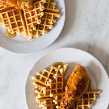 White plates of chicken and waffles on a marble countertop.