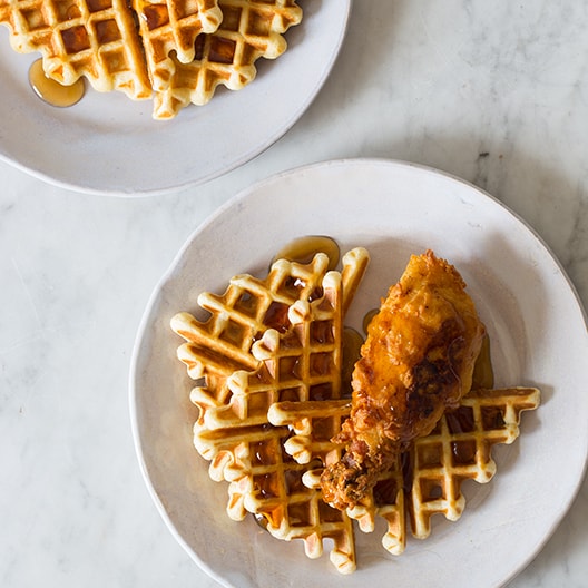 Chicken and waffles on two plates with maple syrup on top. 