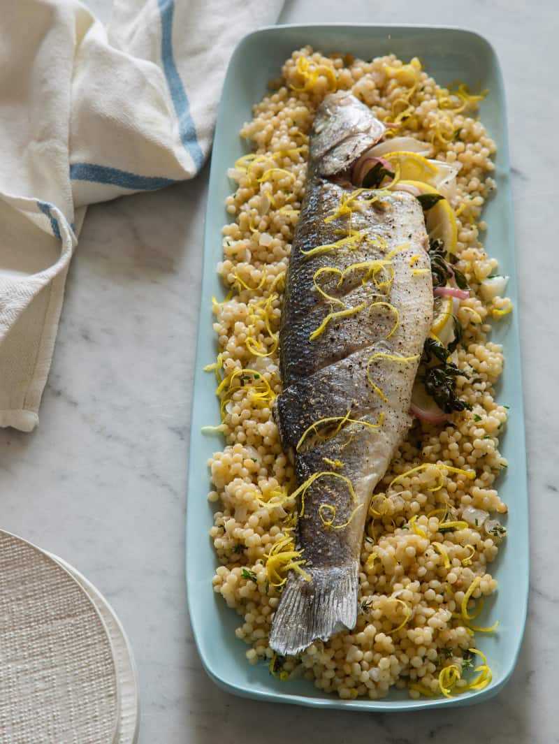 A platter of oven roasted branzino on a bed of cous cous. 