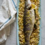 A blue platter of whole roasted branzino on herbed Israeli couscous.