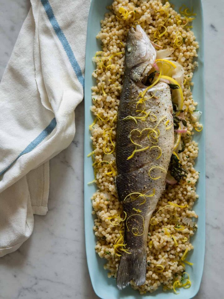 A blue platter of whole roasted branzino on herbed Israeli couscous.
