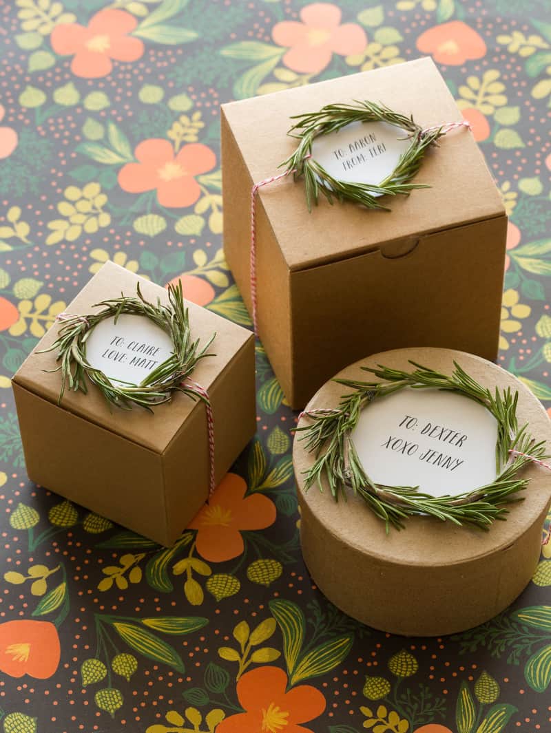 Rosemary wreath gift toppers tied to varying size and shaped brown gift boxes.