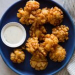 Baby bloomin' onions on a dark blue plate with a side of buttermilk ranch dipping sauce.