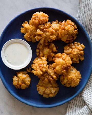 Baby bloomin' onions on a dark blue plate with a side of buttermilk ranch dipping sauce.