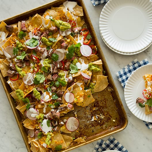 A baking sheet of Carne Asada Nachos with plates on the side and napkins. 