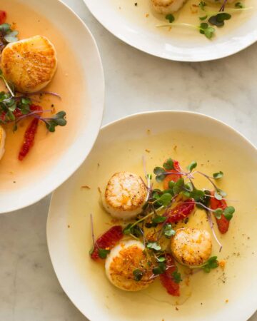 Plates of citrus seared scallops garnished with blood orange segments and micro greens.
