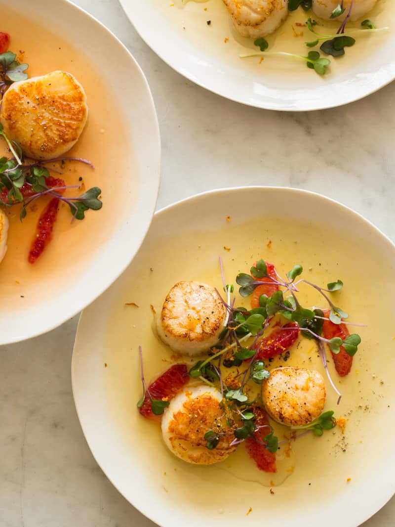 Plates of citrus seared scallops garnished with blood orange segments and micro greens.