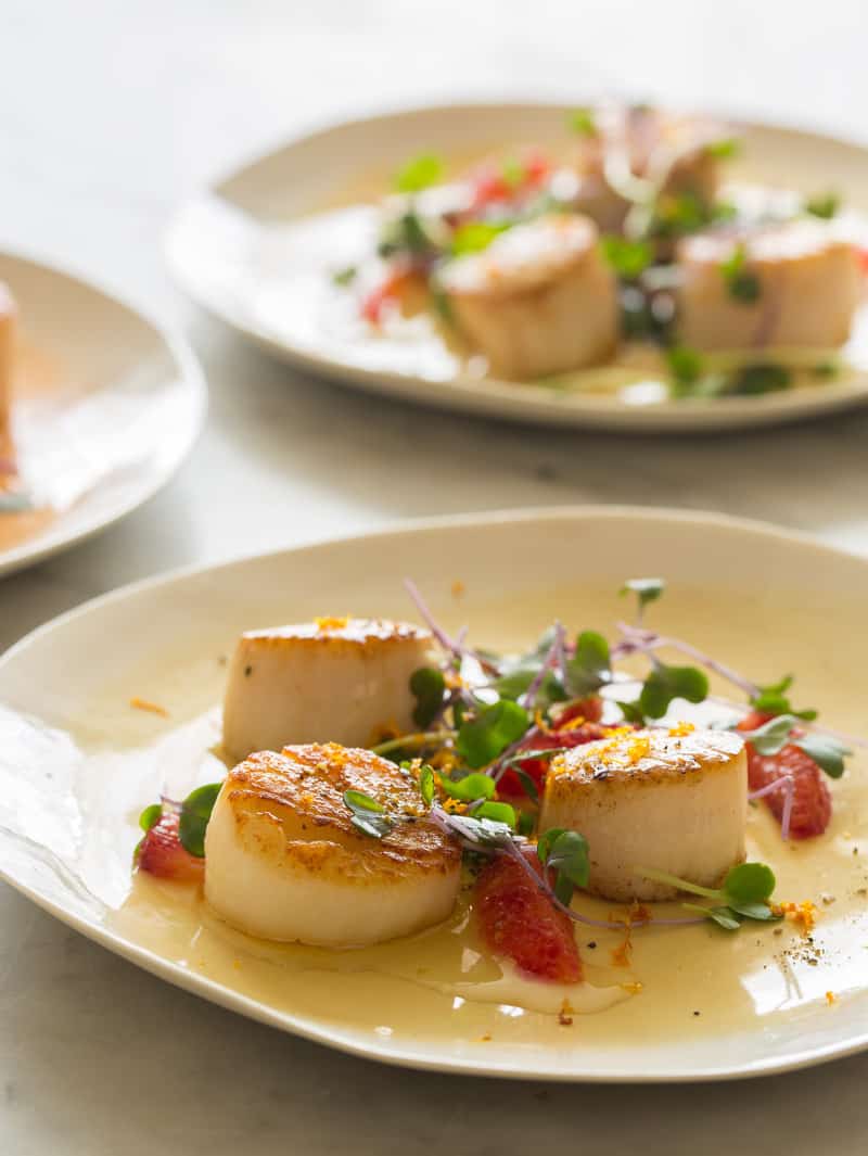 A plate of citrus seared scallops with another plate in the background. 