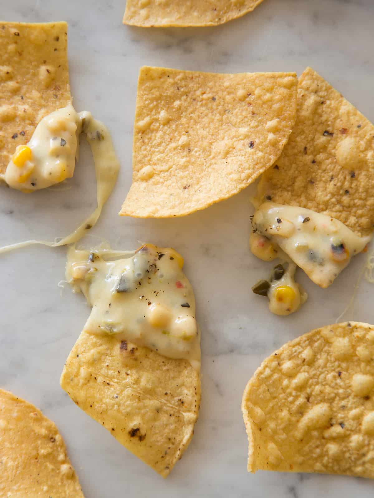 A close up on tortilla chips with some dipped in the queso on a kitchen counter. 
