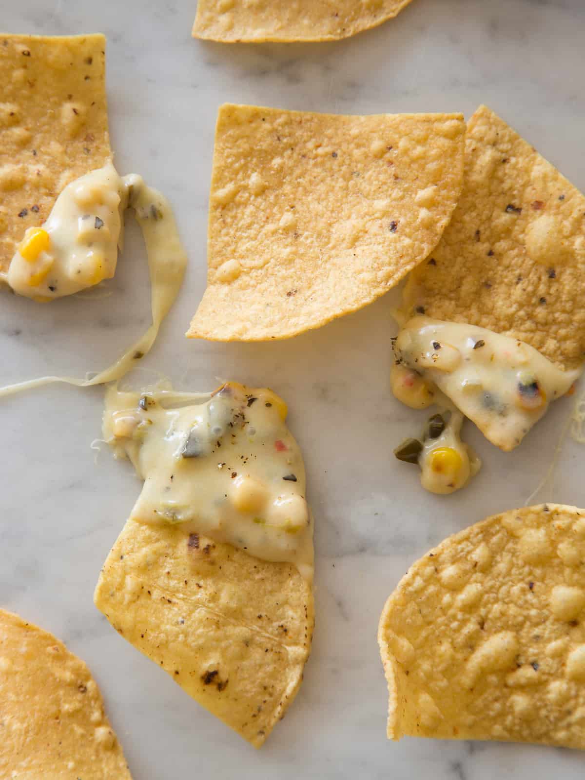 A close up on tortilla chips with some dipped in the queso on a kitchen counter.
