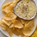 A bowl of roasted poblano queso fondido on a plate of tortilla chips.