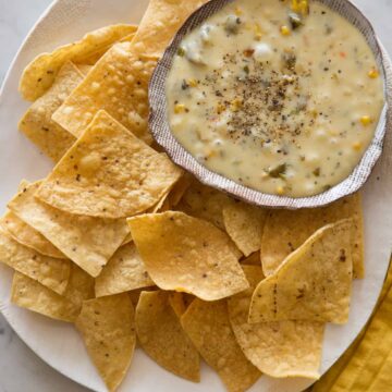 A bowl of roasted poblano queso fondido on a plate of tortilla chips.