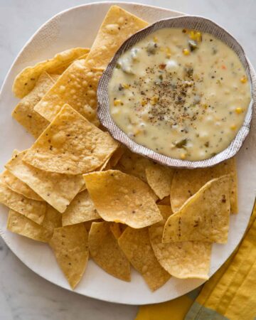 A bowl of roasted poblano queso fondido on a plate of tortilla chips.