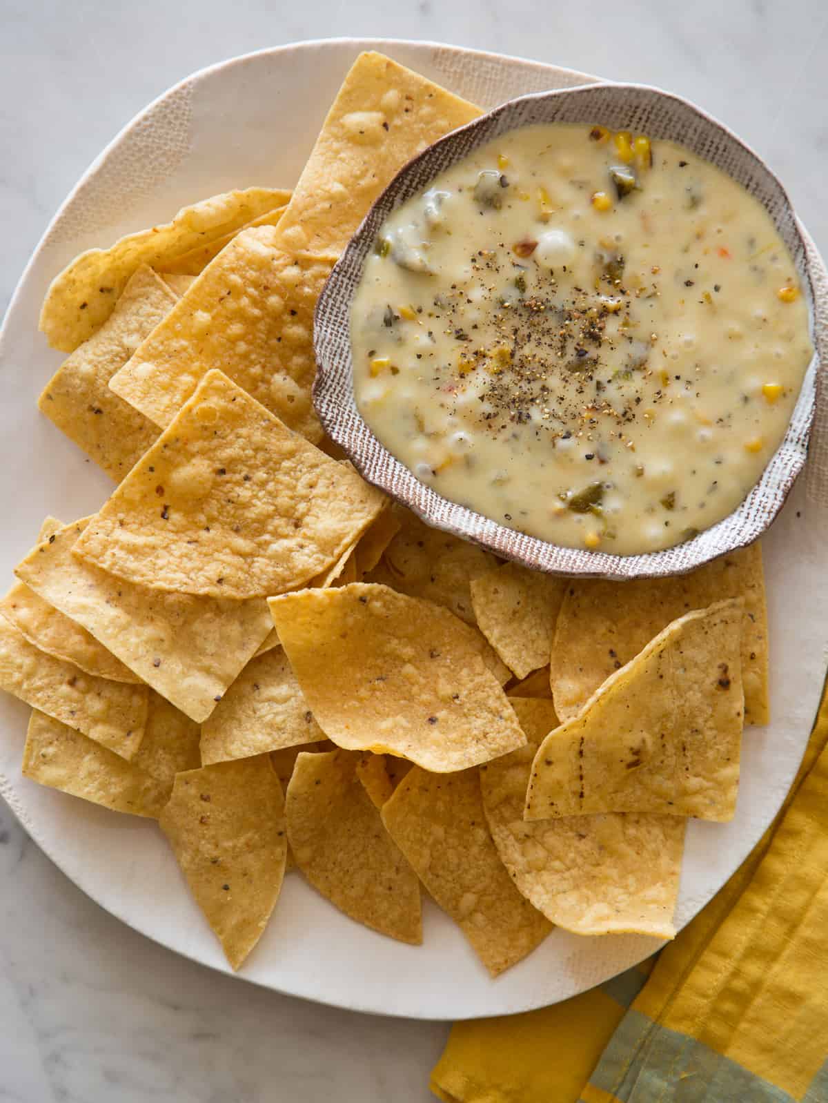 A bowl of roasted poblano queso fondido on a plate of tortilla chips.