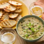 A bowl of roasted broccoli and white cheddar queso fundido with crostini and drinks.