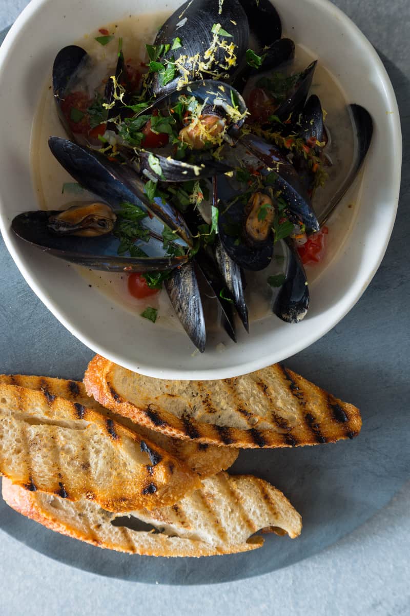 A bowl of white wine steamed mussels with a stack of grilled bread next to it. 