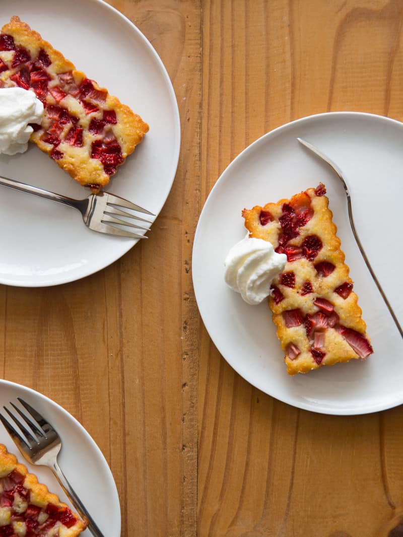 Mini strawberry cobblers on plates with forks topped with whipped cream. 