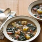 Bowls of hearty white bean and kale soup with napkins and spoons.