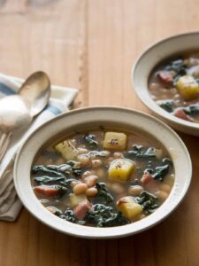Bowls of hearty white bean and kale soup with napkins and spoons.