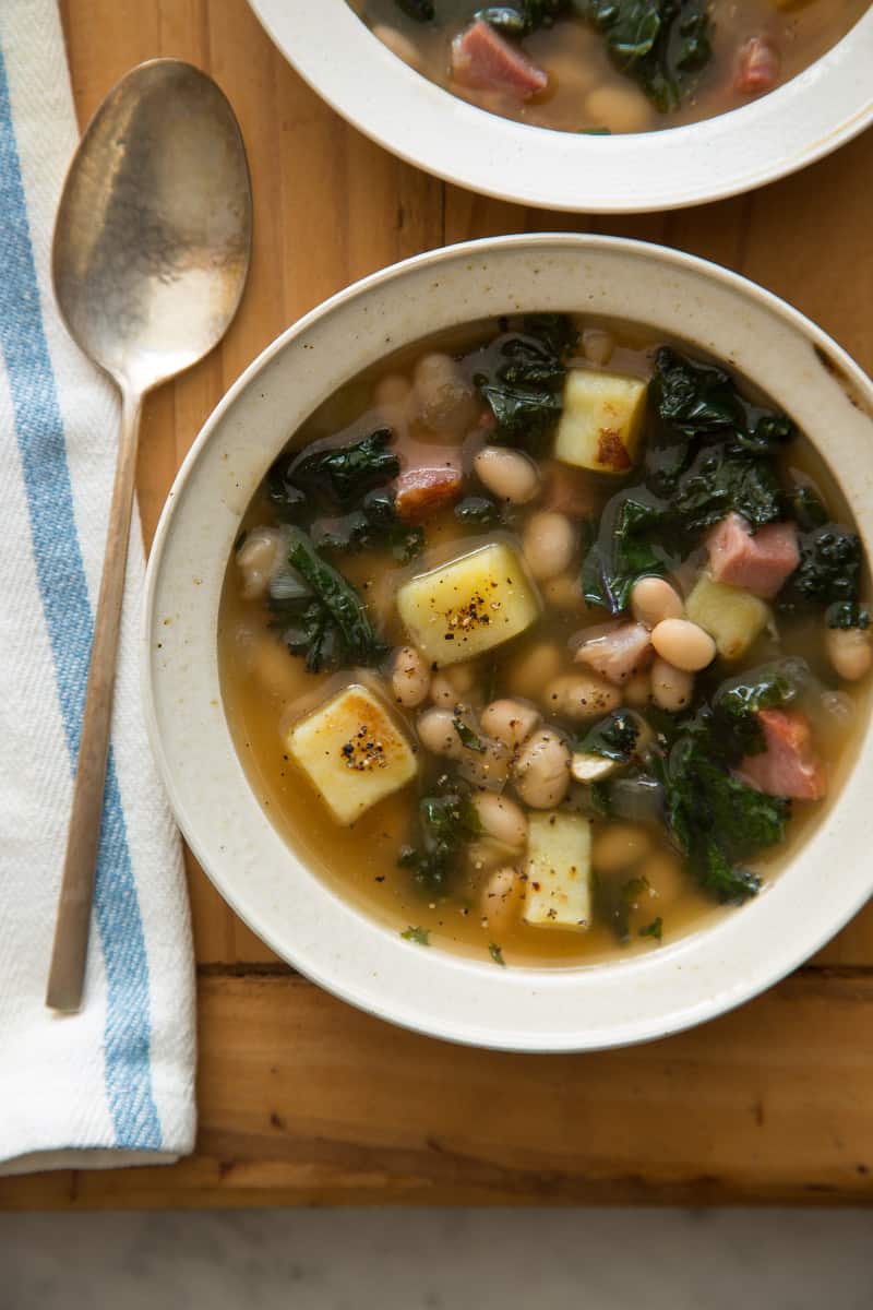 Two bowls of kale and white bean soup with a spoon next to one of the bowls.