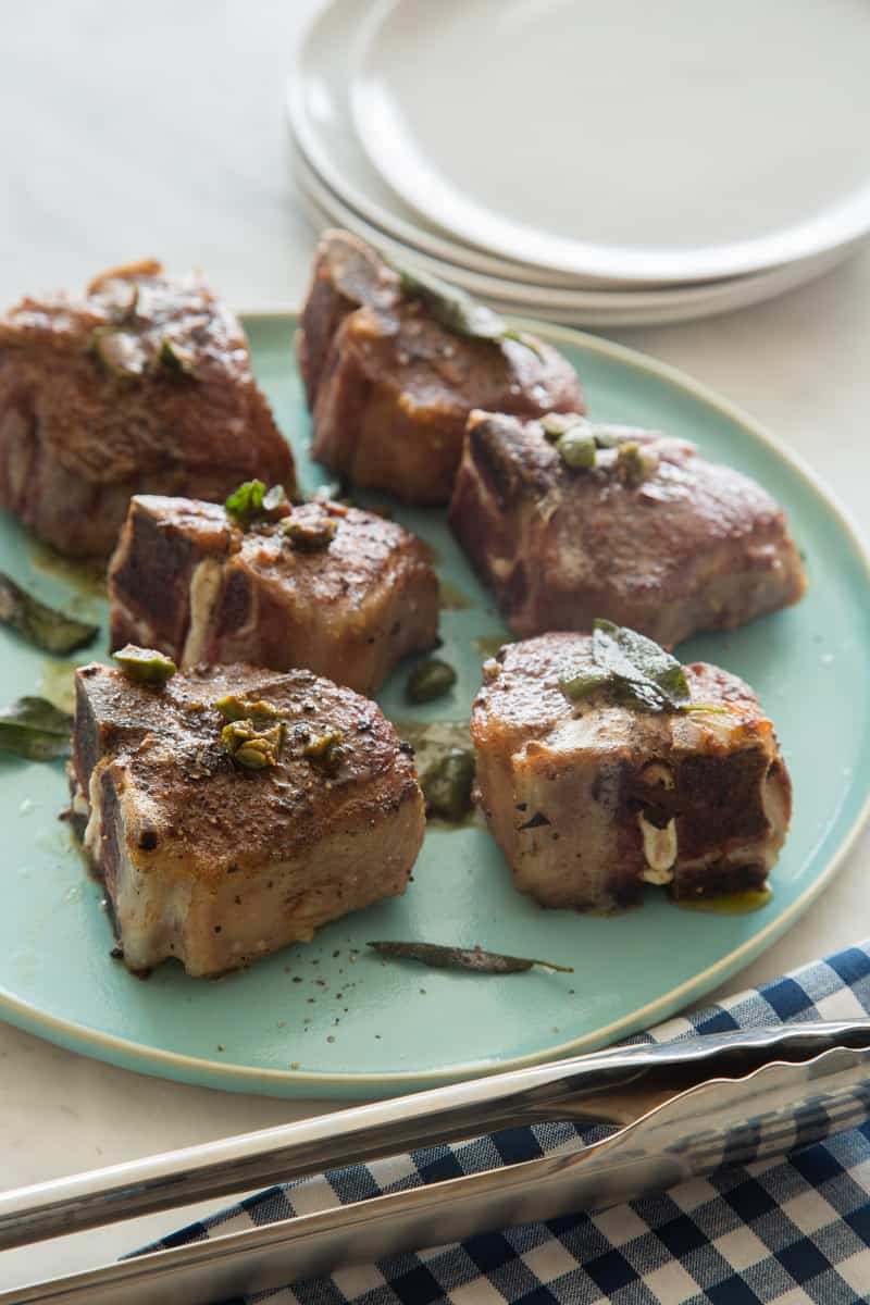 A plate of garlic and anchovy lamb chops with a stack of plates next to it. 
