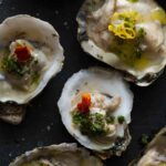 A close up of roasted oysters with a variety of garnish.