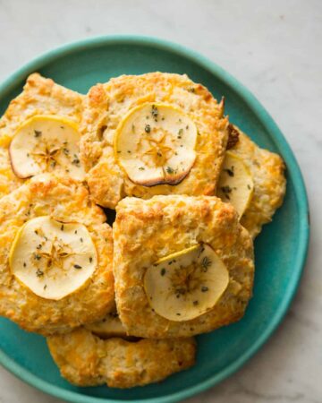 Apple cheddar scones piled on a blue green plate.