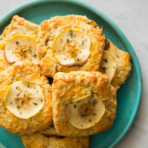 Apple cheddar scones piled on a blue green plate.