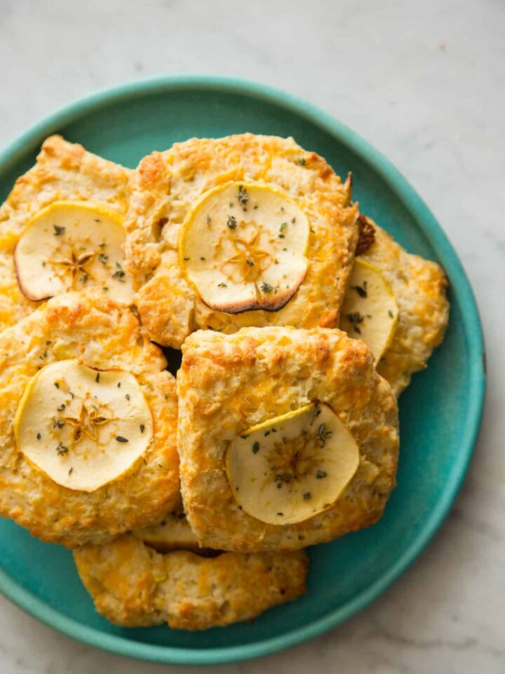 Apple cheddar scones piled on a blue green plate.