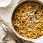 One pot pasta with sausage and zucchini with plates and tongs.